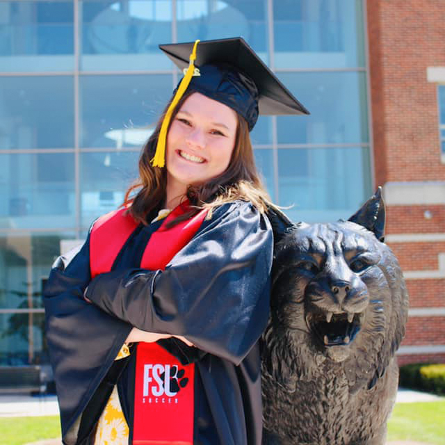 Gwen A. Schemm ingraduation attire with bobcat statue